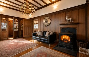 A cozy living room with a fireplace, a leather sofa, patterned rugs, and wooden paneling. - Balvonie House, Grand Scottish Mansion, Hot Tub with Island Views. 12 Bedrooms (Skelmorlie)