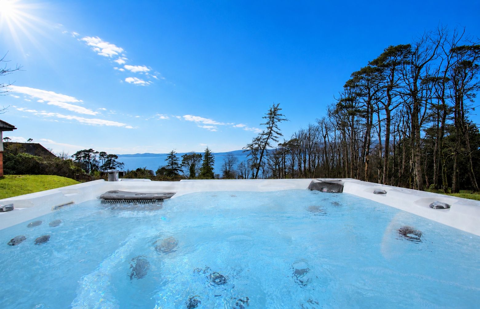 A hot tub with a clear view of the surrounding landscape, including trees and a distant body of water.