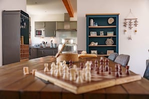 A dining area with a chessboard, a wooden table, and a teal-colored shelving unit with decorative items. - Cool Waves: A fab contemporary holiday home in Rhosneigr (Rhosneigr)