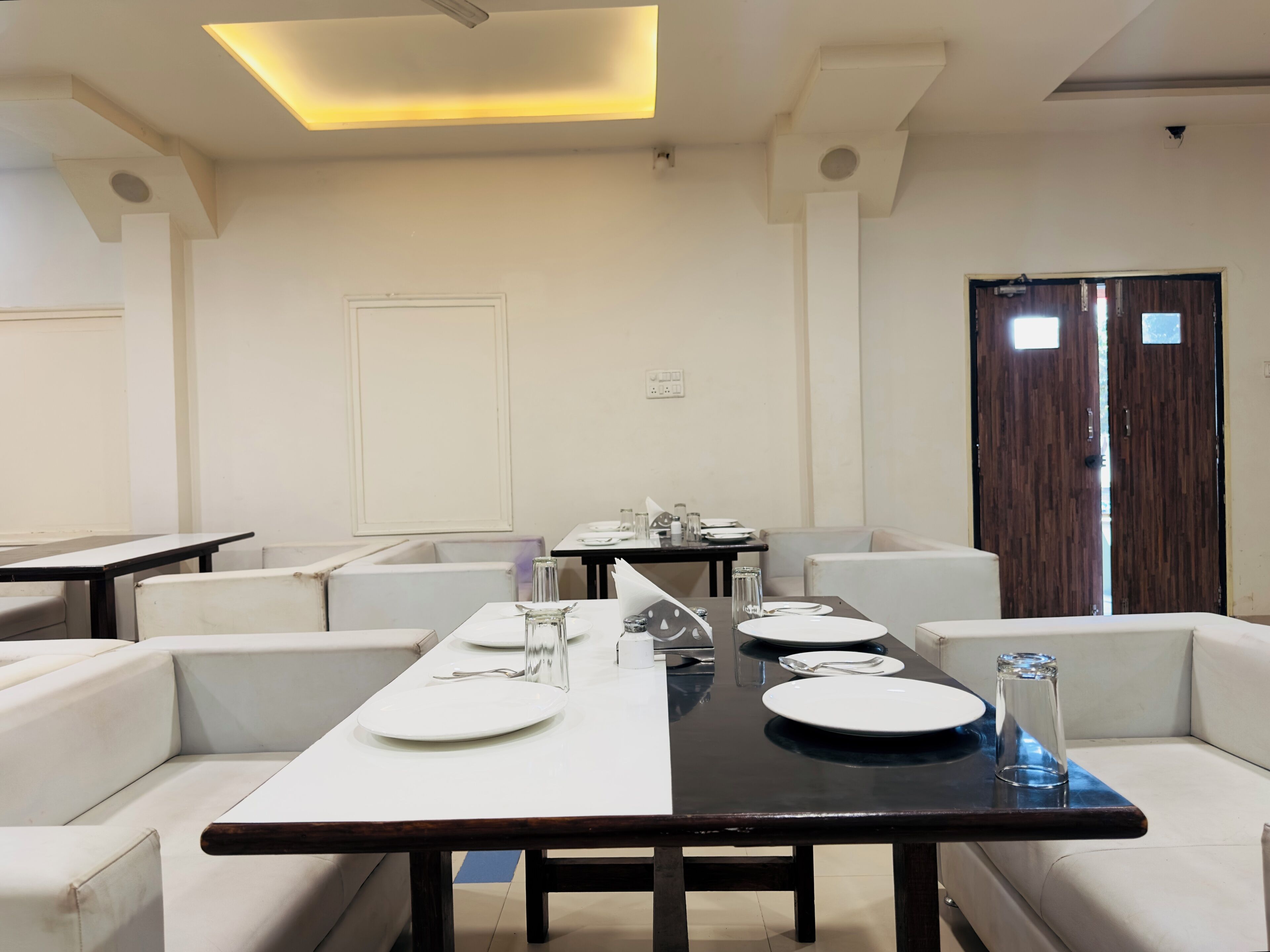 A modern dining area with a long table, white cushioned seating, and a dark wooden table.