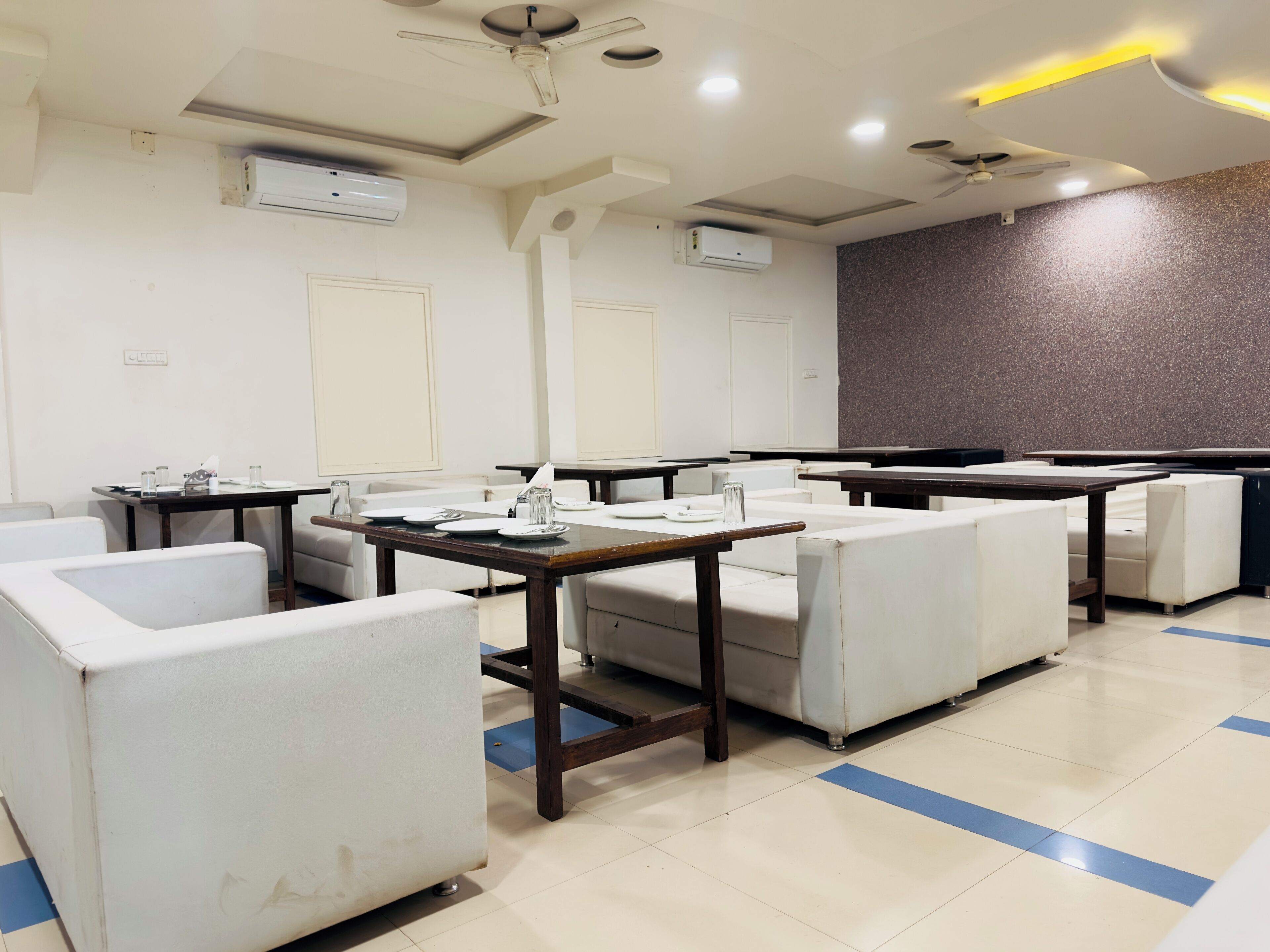 A conference room with white chairs, tables, and air conditioning units on the ceiling.