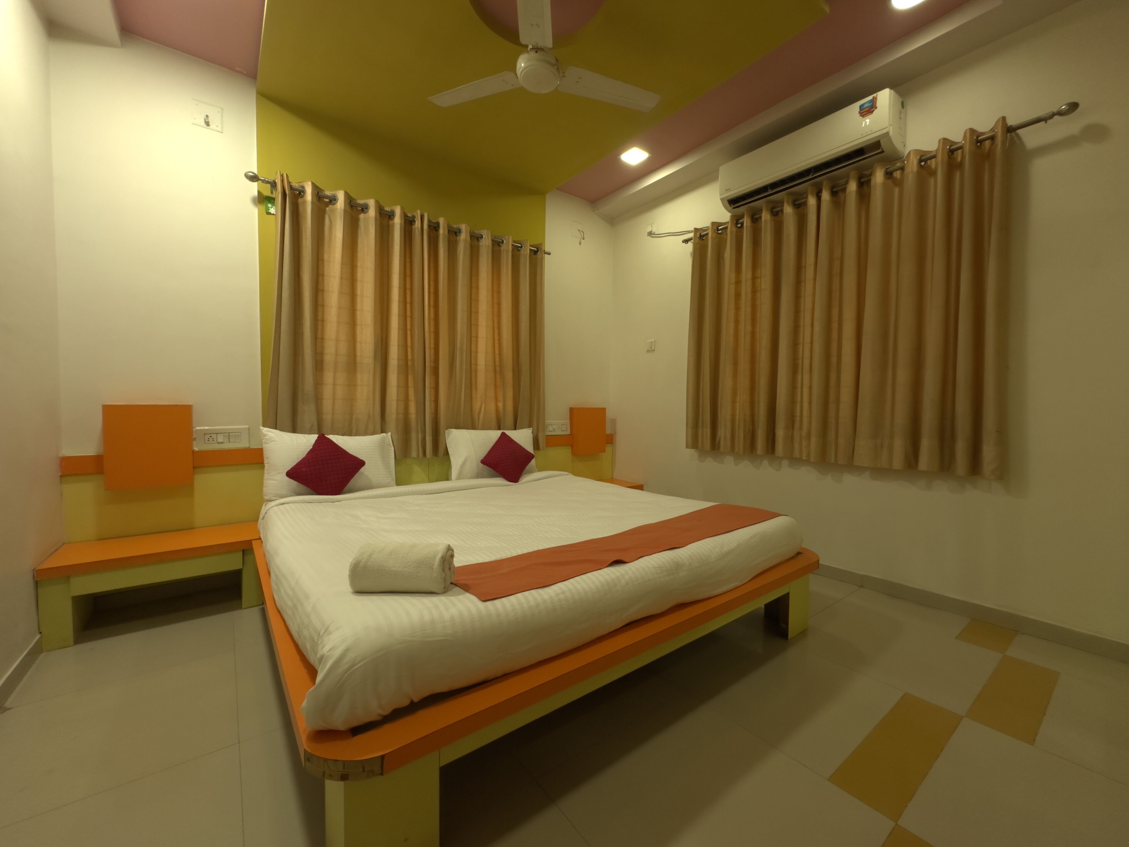 A neatly arranged hotel room with a bed, two bedside tables, a ceiling fan, and an air conditioning unit.