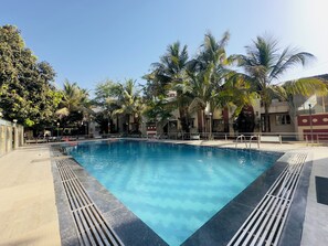 Ein rechteckiger Swimmingpool mit klarem, blauem Wasser, umgeben von Palmen und einer gefliesten Liegefläche.