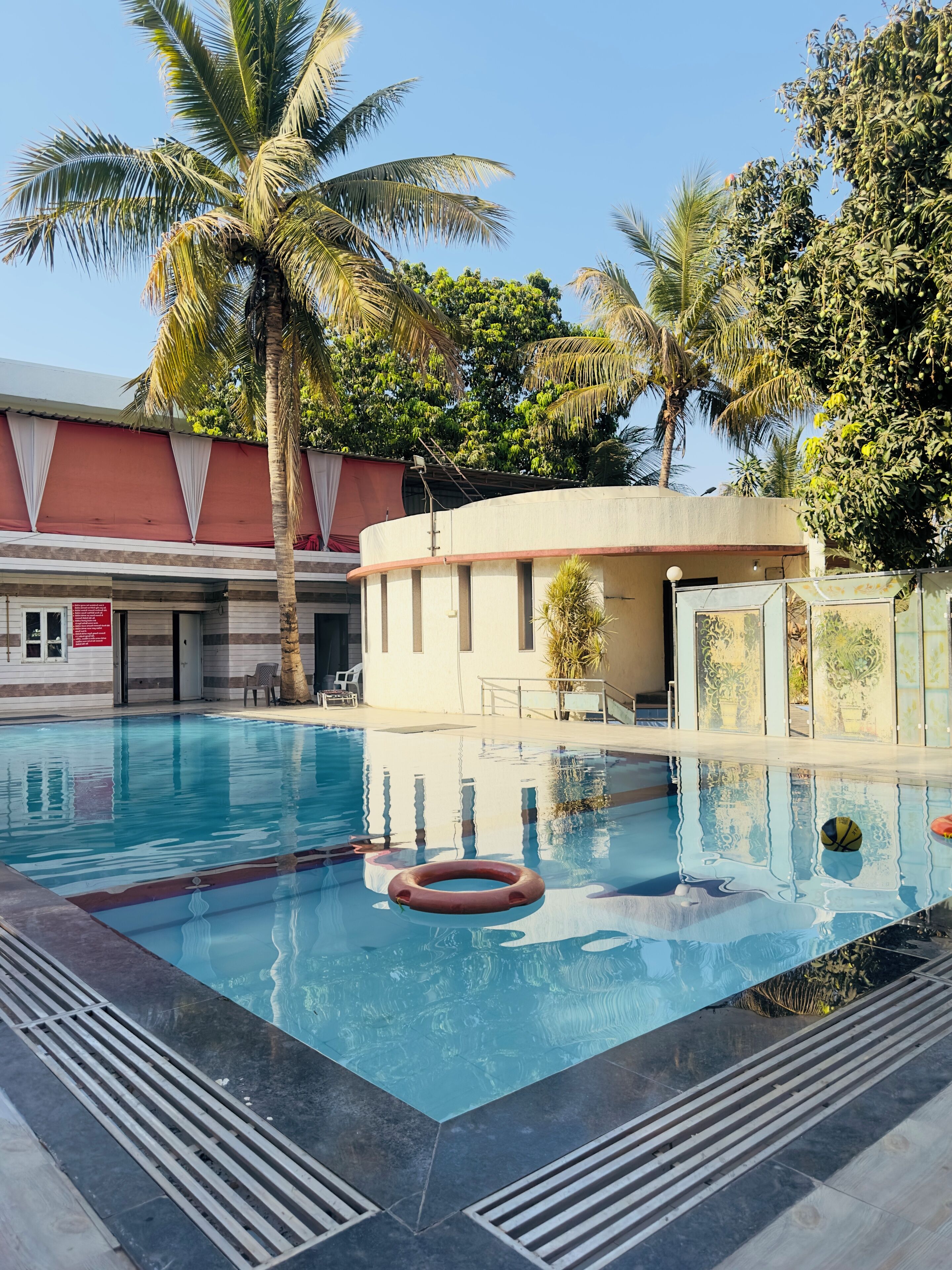 A swimming pool with clear water, surrounded by palm trees and a building with a red and white facade.