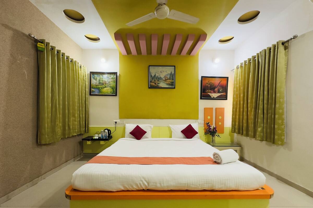 Ein Hotelzimmer mit einem großen Bett, grünen Vorhängen, einem Deckenventilator und Kunstwerken an den Wänden.