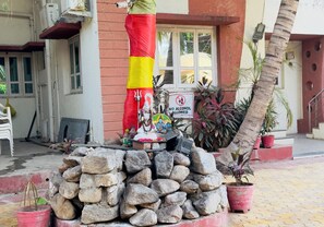 Ein Steinaltar mit Statue, ein Verbotsschild für Alkohol und Blumentöpfe vor einem Gebäude.