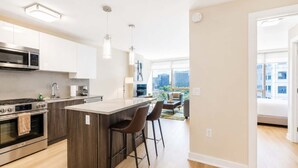 A modern kitchen with a central island, stainless steel appliances, and a dining area with a view. - Luxury Apt Near Downtown (Stamford, CT)