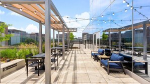 An outdoor patio area with tables and chairs, string lights, and a view of the cityscape. - Luxury Apt Near Downtown (Stamford, CT)