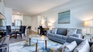 A modern living room with a glass coffee table, grey sofa, and a dining area with chairs and a table. - Luxury Modern Apt with Patio (Lexington, MA)