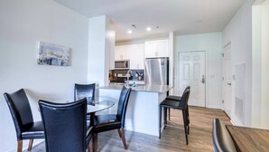 A modern kitchen with white cabinets, a stainless steel refrigerator, and a dining area with a glass table and black chairs. - Luxury Modern Apt with Patio (Lexington, MA)