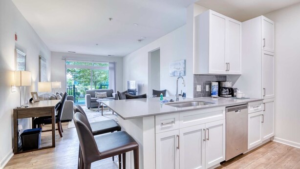 A modern kitchen with white cabinetry, a central island, and a dining area with a table and chairs. - Luxury Modern Apt with Patio (Lexington, MA)