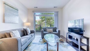 A modern living room with a grey sofa, a glass coffee table, and a flat-screen TV on a wooden stand. - Luxury Modern Apt with Patio (Lexington, MA)