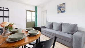 A modern living room with a grey sofa, a wooden dining table with plates and cutlery, and a green curtain.