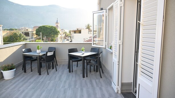 Un balcone con tavolo e sedie, una pianta in vaso e vista su una montagna e degli edifici.