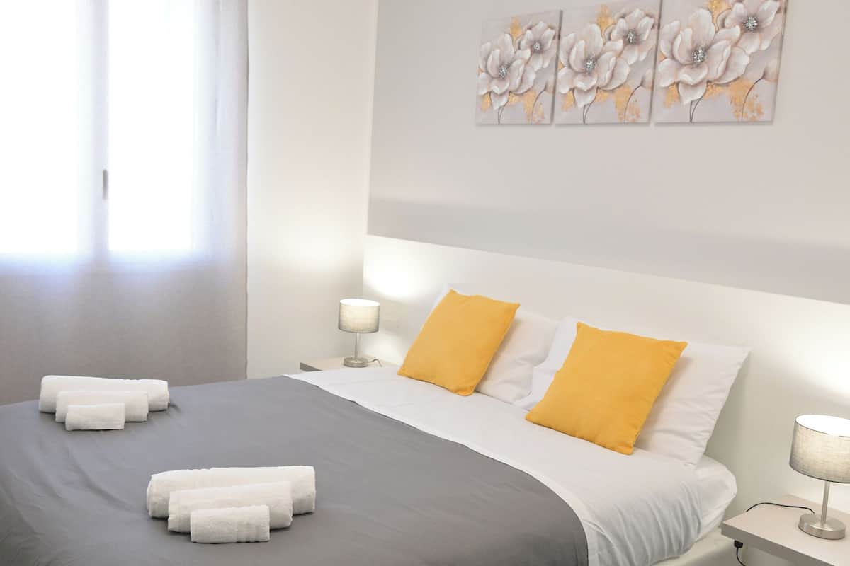 A modern bedroom with a large bed, two bedside lamps, and a window with curtains.