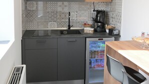 Una cucina compatta con forno a microonde integrato, macchina del caffè e frigorifero.