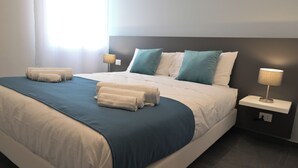 Un letto rifatto con una coperta azzurra e bianca, due asciugamani bianchi e una lampada da comodino su un tavolino.