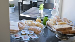 Un balcone con un tavolo apparecchiato per un pasto, con panini e bevande, affacciato su una città con edifici e una montagna.