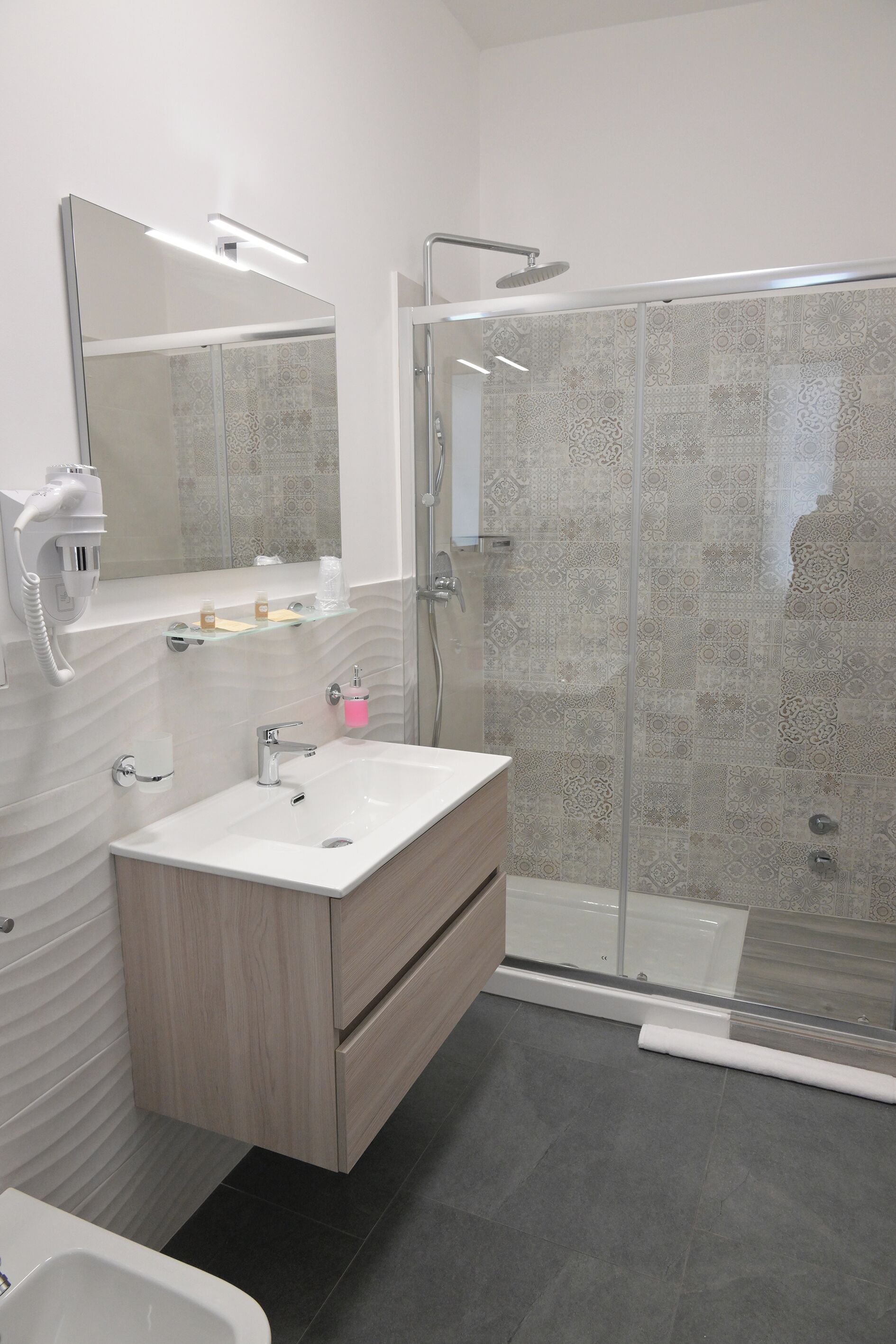 A modern bathroom with a glass-enclosed shower, a white sink, and a vanity with a mirror.