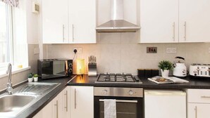 A modern kitchen with white cabinets, a gas stove, a microwave, and a toaster. - Charming fully furnished 2-bedroom home (Nottingham)