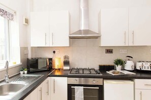 A modern kitchen with white cabinets, a gas stove, a microwave, and a toaster. - Charming fully furnished 2-bedroom home (Nottingham)
