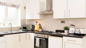 A modern kitchen with white cabinets, a stove, a microwave, and a toaster. - Charming fully furnished 2-bedroom home (Nottingham)