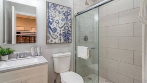 A modern bathroom with a glass shower enclosure, a white toilet, and a sink with a mirror above it. - Suite 2 on Southport 4 Queen Beds (Chicago)