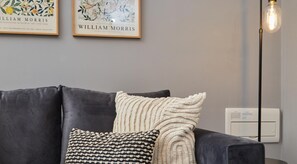 Relax in a stylish living room with a dark grey sofa, framed artworks by William Morris, and a floor lamp.