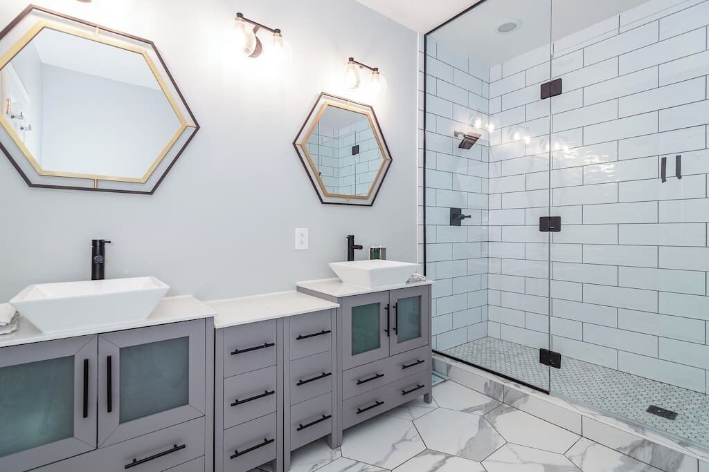 A modern bathroom with two sinks, a shower, and hexagonal mirrors.