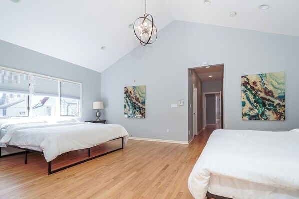 A modern bedroom with two beds, a chandelier, and abstract wall art.