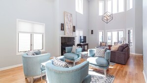 Ein geräumiges Wohnzimmer mit Kamin, mehreren Sitzbereichen und großen Fenstern, die für natürliches Licht sorgen.