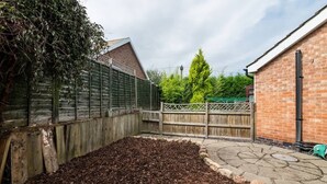 Un pati amb una tanca de fusta, un edifici de maó i una zona de jardí amb mulch.
