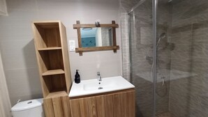 Een badkamer met een houten wastafelmeubel, een witte wastafel, een spiegel en een douchecabine met glazen wanden.