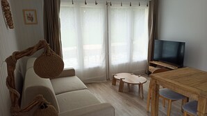 Een woonkamer met een bank, een televisie, een houten tafel en een raam met gordijnen.