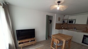 Een moderne woonkamer met een flatscreen televisie, houten meubels, een eettafel en een keuken met een magnetron en spoelbak.