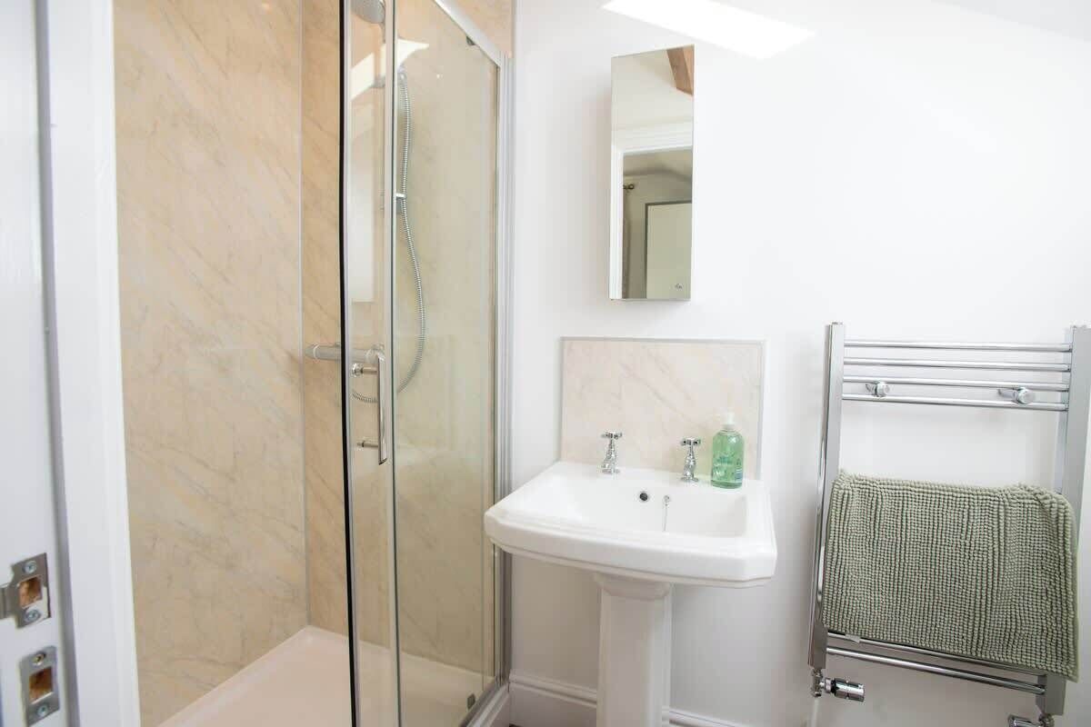 Un baño con cabina de ducha de vidrio, lavamanos pedestal y perchero.