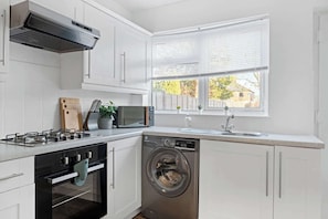 A modern kitchen with a gas stove, oven, microwave, dishwasher, and a window with blinds. - Spacious and Bright Home | Perfect for Contractors (Nottingham)