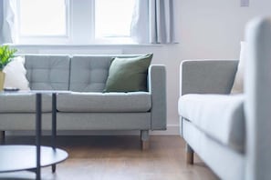 A modern living room with a grey sofa, a round table, and a window with curtains.