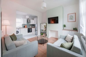 A modern living room with grey sofas, a coffee table, and a TV mounted on the wall.