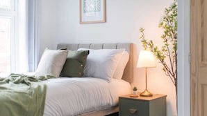A neatly made bed with pillows, a bedside lamp, a small plant, and a framed picture on the wall.