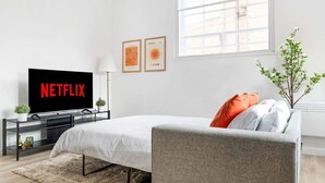 Une chambre à coucher moderne avec un lit, un téléviseur affichant le logo « NETFLIX », une fenêtre et une plante.
