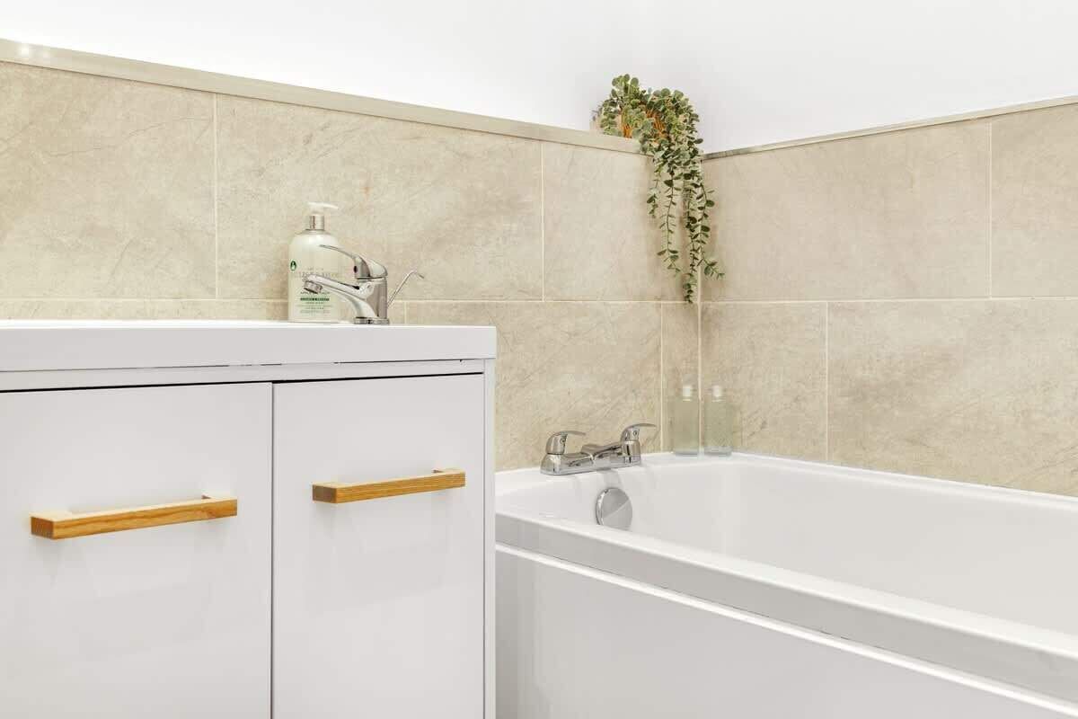 A bathroom with a white bathtub, a wooden cabinet with drawers, and a plant on the wall.