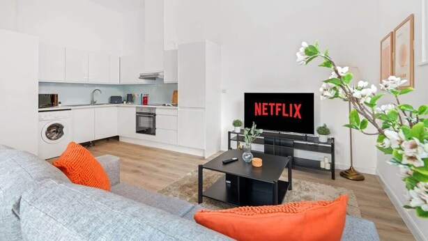 Un salon moderne avec un canapé gris, une table basse et un téléviseur affichant le logo « NETFLIX ».
