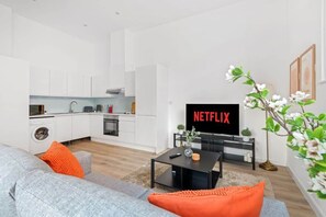 Moderni olohuone, jossa on harmaa sohva, sohvapöytä ja televisio, jonka näytöllä näkyy teksti ”NETFLIX”.