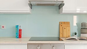 Une cuisine équipée d’une cuisinière intégrée, d’une planche à découper et de quelques livres posés sur le comptoir.