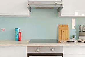 Una cocina con estufa integrada, tabla de cortar y algunos libros en la encimera.