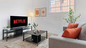 Un salon avec un téléviseur, une table basse, un canapé, une lampe et une fenêtre.