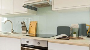 Een moderne keuken met een inbouwoven, een roestvrijstalen afzuigkap, een messenblok, een snijplank en een koffiezetapparaat.