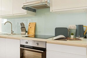 Une cuisine moderne équipée d’un four encastré, d’une hotte en acier inoxydable, d’un bloc à couteaux, d’une planche à découper et d’une machine à café.