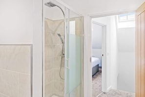 A bathroom with a glass-enclosed shower, a visible door leading to a bedroom, and a tiled floor. - Warm and Inviting Apartment | Free Parking (Newark-on-Trent)